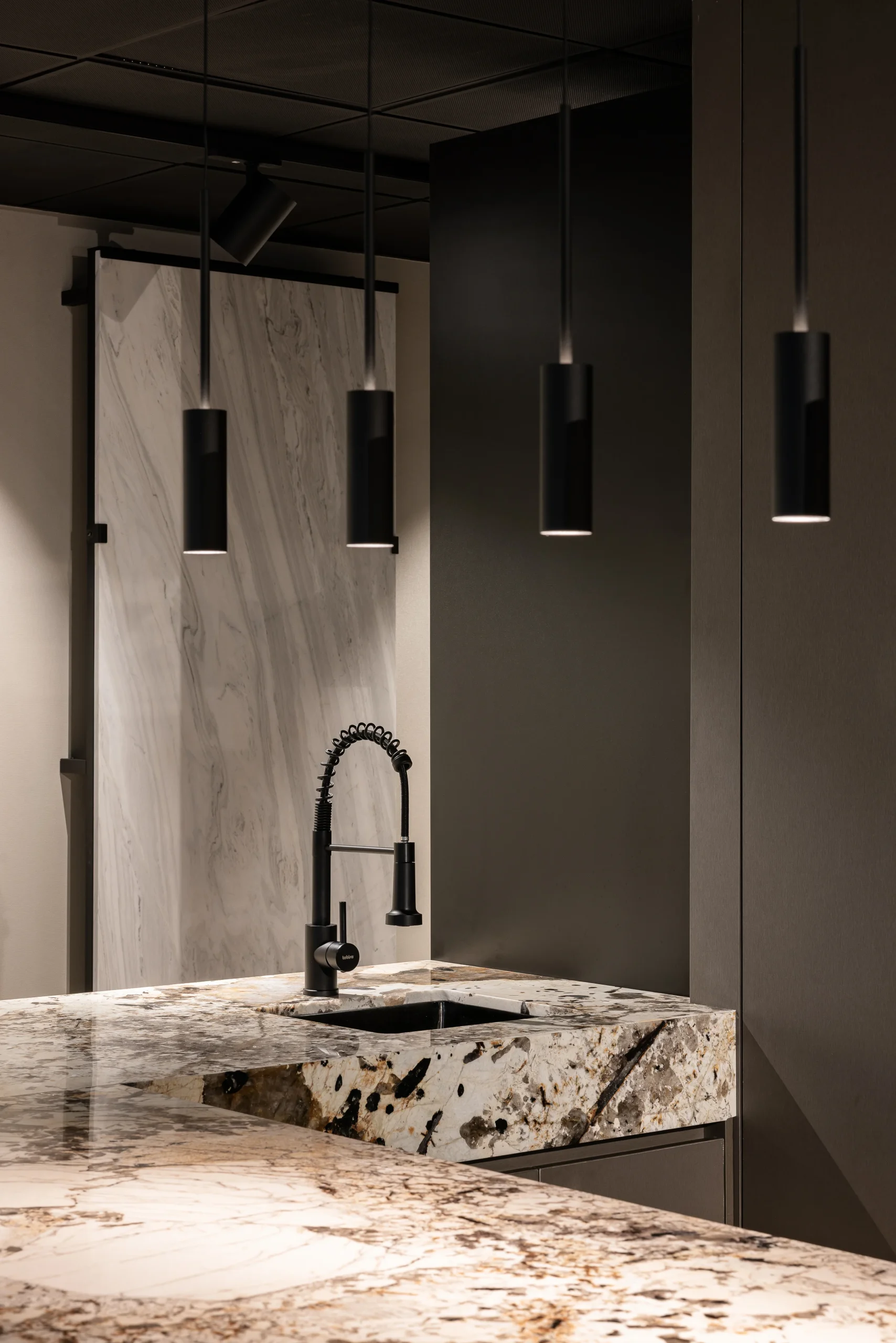Mesón de piedra natural con grifo negro y luminarias colgantes en showroom