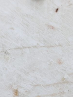 Detalle de superficie de cuarcita Cristallo Exótica blanca con vetas beige cálidas e inclusiones oscuras.