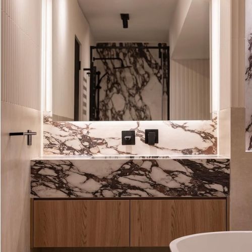 Mesón de baño en Ultracompacto Creastone Calacatta Viola con espejo retroiluminado, grifería negra mate y muebles de madera, proyecto Carmen Sylva